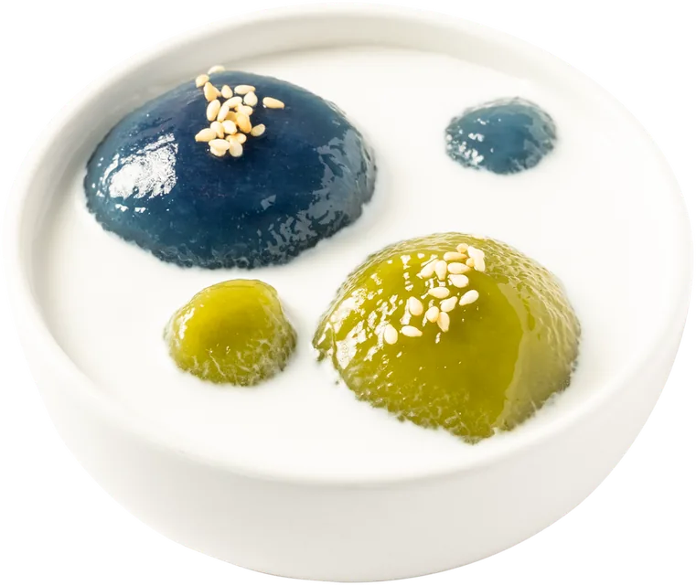 Bowl of blue and green mochi balls in coconut cream with sesame seeds